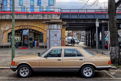 Gold Mercedes-Benz W126 parked on a road