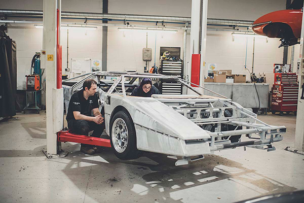Two mechanics working inside an Aston Martin Bulldog chassis in a garage