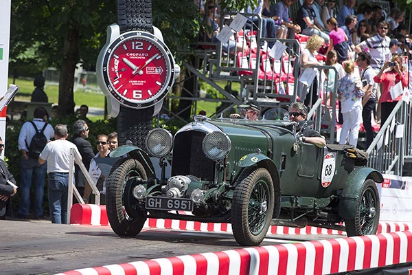 A green classic Bentley on a sunny day taking part in a car race with spectators in the background