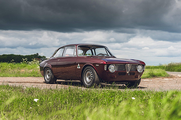 Metallic Dark Red Alfaholics Gta R 029  on a meadow lined country road Courtesy Alfaholics