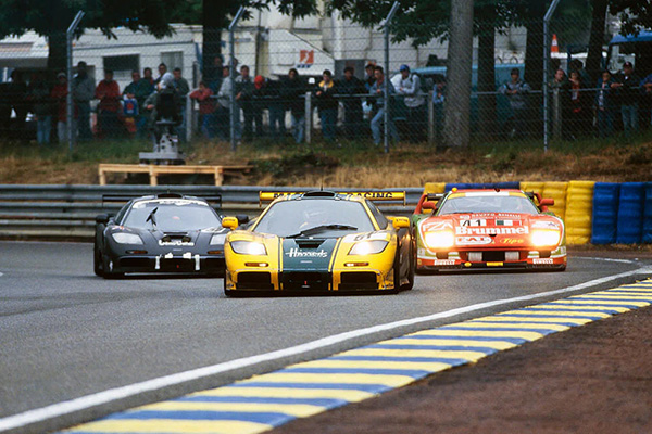 Three 1995 Mclaren F1 GTR's Racing Around racetrack bend watched by Spectators Behind Wire Fence