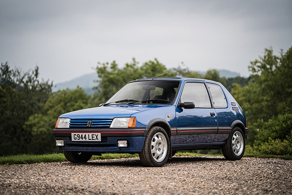 Blue 1990S Peugeot 205 GTi on gravel with trees and mountain backdrop