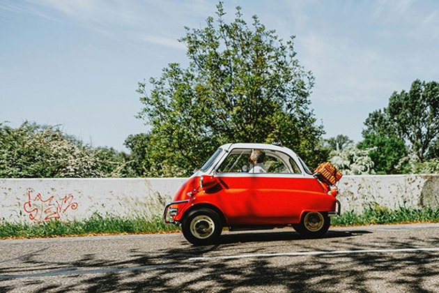 An orange microcar driving along a sunny road