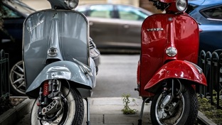 A silver and a red Vespa parked side by side on a pavement