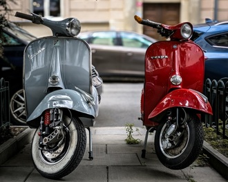 A silver and a red Vespa parked side by side on a pavement