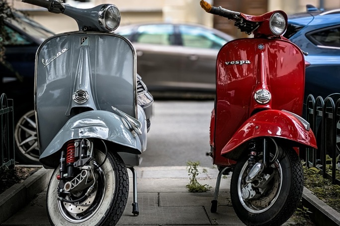 A silver and a red Vespa parked side by side on a pavement