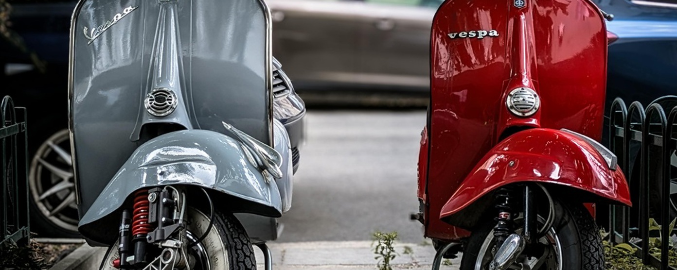 A silver and a red Vespa parked side by side on a pavement