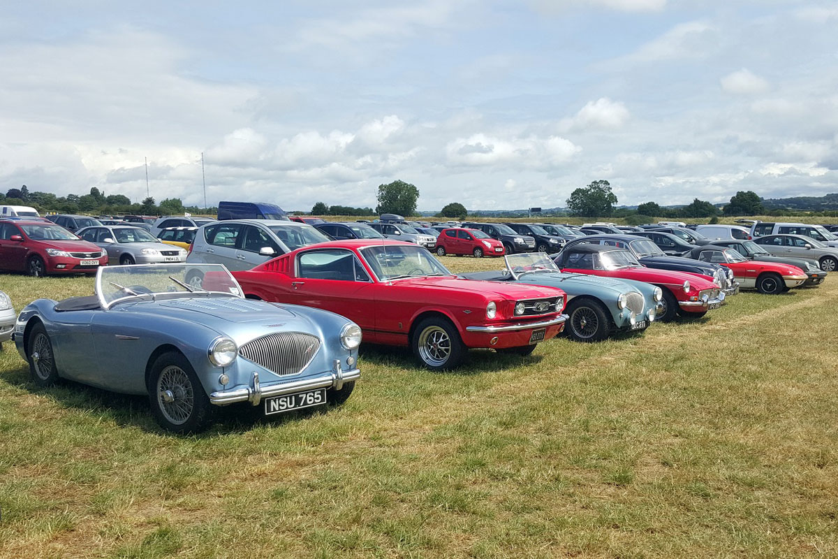 1955 blue Austin Healey next to Ford Mustang and other vehicles