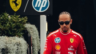 Lewis Hamilton walking towards the camera wearing a red t shirt and sunglasses