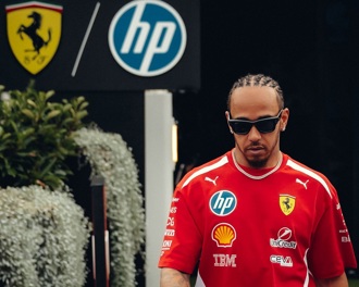Lewis Hamilton walking towards the camera wearing a red t shirt and sunglasses