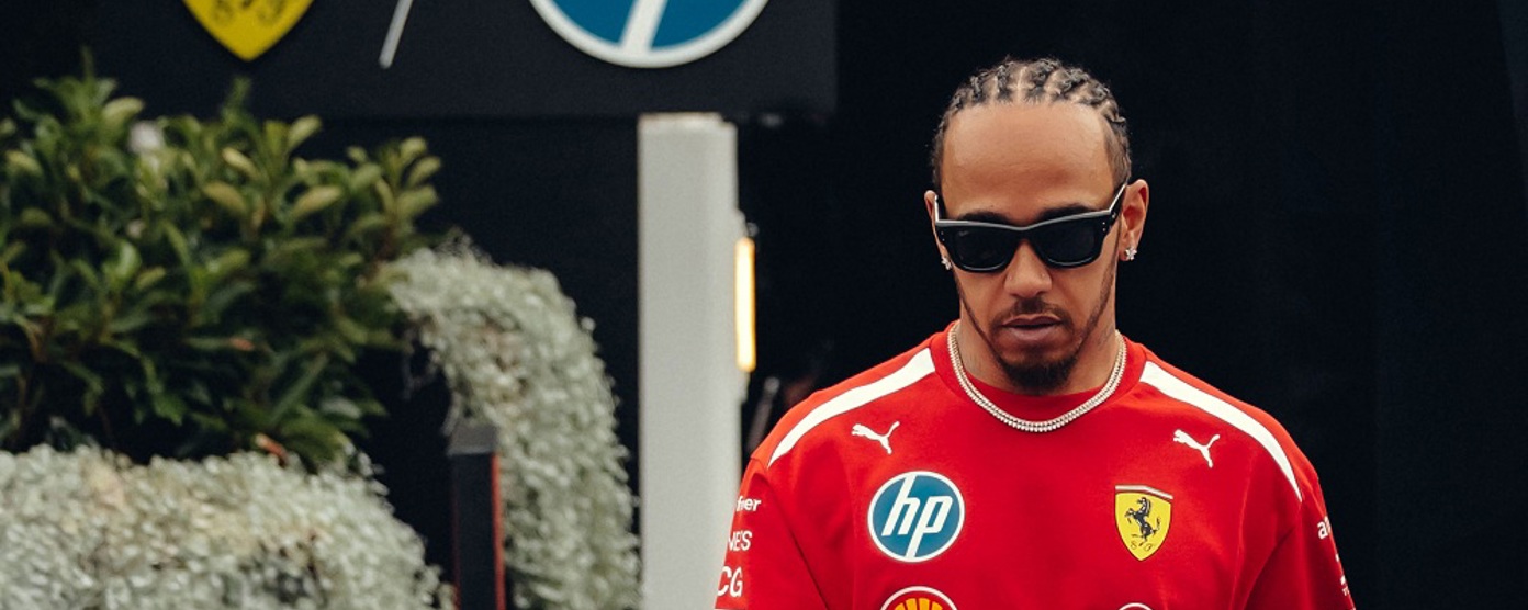 Lewis Hamilton walking towards the camera wearing a red t shirt and sunglasses