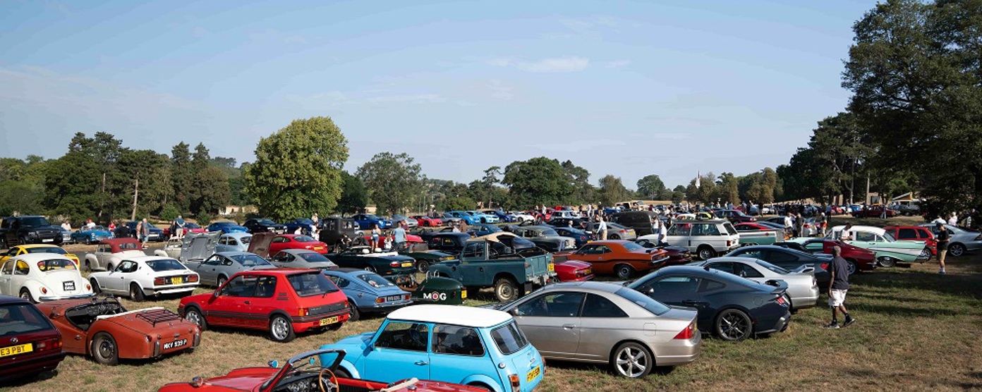 Rows of classic cars in a sunny field at a car show