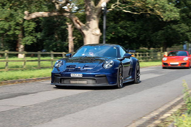 dark-blue-porsche-911-driving-beside-grass-and-trees
