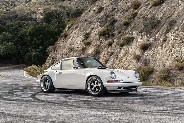 Cream Singer Porsche 911 on a tire marked road with a mountain backdrop