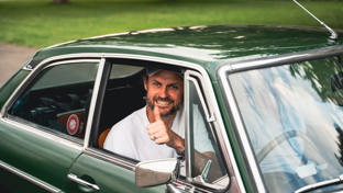 A man in a baseball cap smiling in a green MG