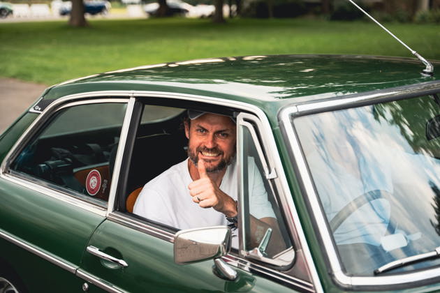 A man in a baseball cap smiling in a green MG