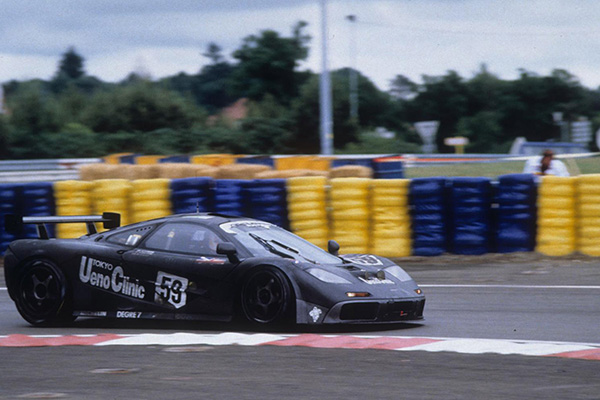 Dark Metallic 1995 Mclaren F1 GTR On Racetrack racing past colour tire barriers - courtesy Aco Le Mans