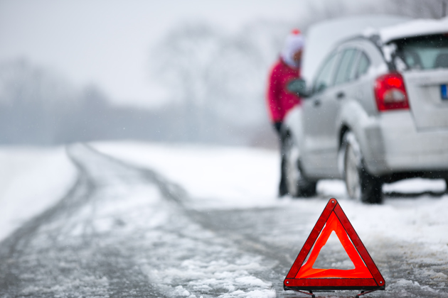 Red warning triangle on a snowy icy road with a broken-down car and driver in the background