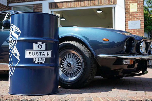 A Sustain Classic Oil Barrel In Front Of a Metallic Blue Aston Martin V8 with an open bio folding doors backdrop