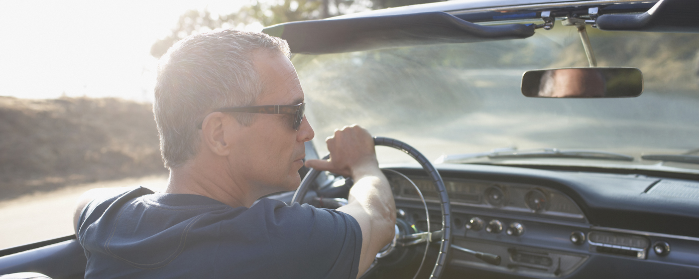 Man wearing sunglasses driving a classic convertible on a sunny day, viewed from the passenger seat