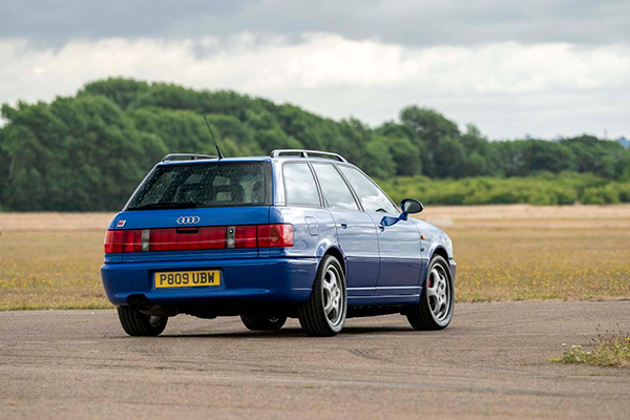 back-view-blue-audi-rs2-avant-driving-on-track-with-fields-and-trees-backdrop