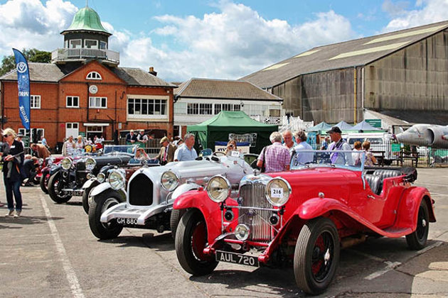 staggered-row-of-silver-1930s-rolls-royce-phantom-ii-red-and-a-black-1933-lagonda-m45-tourer-brooklands-museum-viewing-tower-and-air-craft-hanger