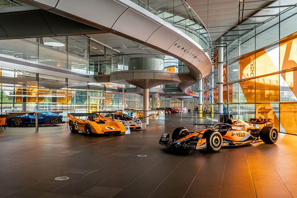 Split Photo Of Mclaren Technology Centre Showroom Sweeping Curves And Glass With Orange Racing Cars And Detroit's Michigan Central Station Beaux Arts Tower Block
