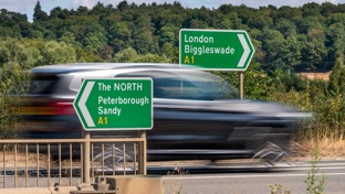 A blurred car speeding past a green motorway sign to London