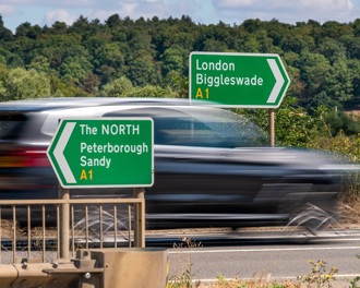 A blurred car speeding past a green motorway sign to London