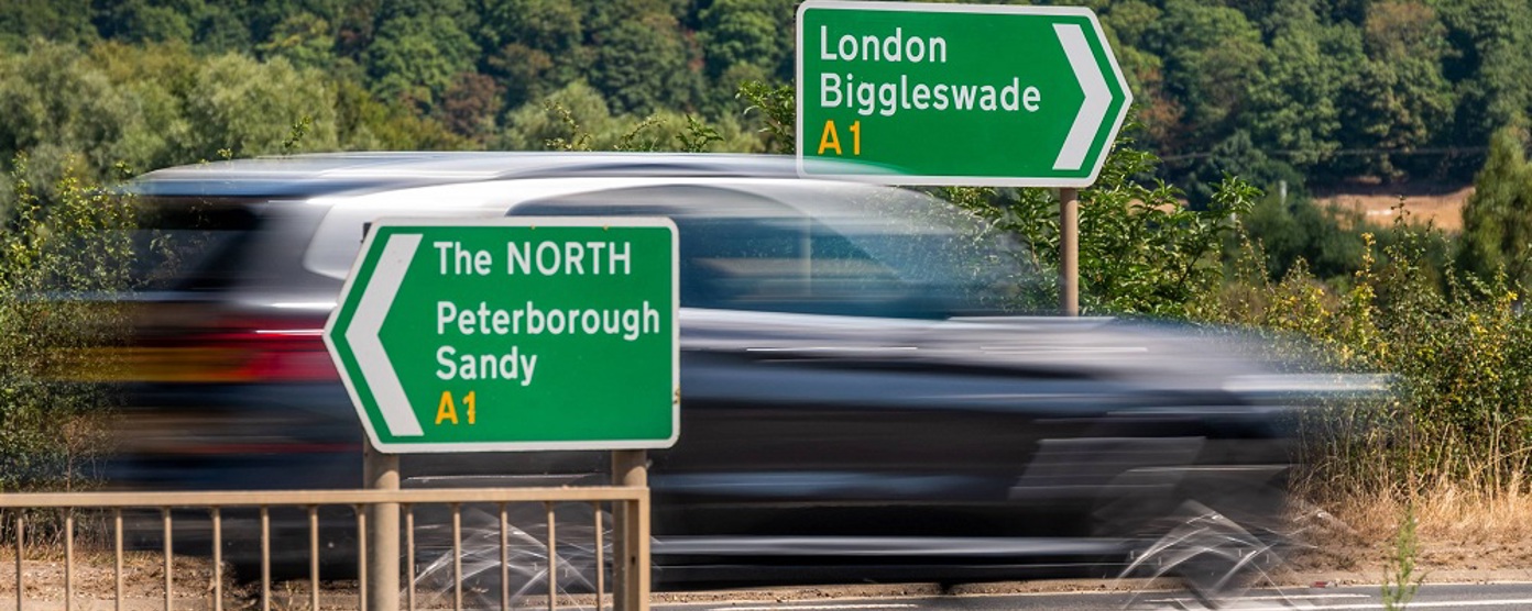 A blurred car speeding past a green motorway sign to London